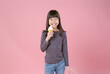 Cute little Asian girl looking at camera and eating ice cream in waffles cone on pink background