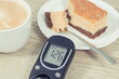 Glucose meter with high result sugar level, portion of sweet cheesecake and cup of coffee with milk. Nutrition during diabetes