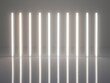 A row of illuminated vertical light tubes in a minimalist setting reflecting on a glossy surface.