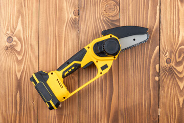 Poster - Small handheld lithium battery powered chainsaw for trimming, cutting trees or bushes branches, on a wooden table background.