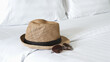 Hat and sunglasses on the white bed. Prepare beach accessories for summer trip.