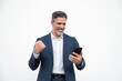 © Stock 4 You - Happy delighted satisfied business man looking at mobile phone screen gesturing yes winning pose, isolated background. Overjoyed excited businessman in suit make winner gesture reading happy good news