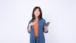 © Jirawatfoto - Asian woman wearing an orange shirt and a denim jacket is celebrating the news on mobile phone against a white background.