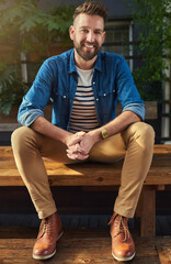 Poster - Portrait, man and smile and relax, bench and casual while bearded, fashion and happy. Confident, travel and vacation in holiday, break and tourist with hands together, restaurant and male person