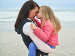 Kiss mother, girl and hug on beach for love, care and relax at ocean in Australia. Single mom, daughter and affection at seaside for security, mothers day and support in nature while happy in cold