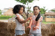 Two young girls, one African-American and one Asian, examine their paint-covered hands together in an outdoor setting.