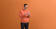 © Moon Safari - Young handsome entrepreneur in eyeglasses messaging over mobile phone on isolated orange background