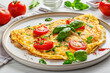 A closeup of the omelette with tomato and green bell pepper, onion and basil leaves on a white plate for breakfast or lunch on a white  background.