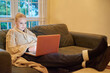 © peopleimages.com - Woman, laptop and streaming on sofa for movie, tv show or entertainment online. Female person, relaxing and browsing internet in living room for downtime, social media and happy on couch in winter