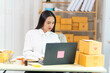 © Uraiwan - woman sit at workplace desk laughing working on-line using laptop in warehouse.