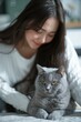 A young woman is sitting on the bed and looking at her British Shorthair cat.