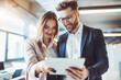 © Volodymyr - Young smiling man and woman in the office looking at the tablet with interest