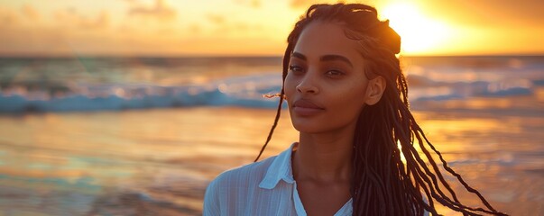 Wall Mural - Beautiful African American woman with long black hair in dreadlocks on an ocean beach during sunset. Wind is blowing her white shirt and hair.