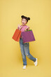 Happy Asian child girl carrying colorful shopping bags walking to supermarket isolated on yellow background.