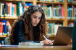 © forenna - young female university or college student studying seriously in a library reading room, using laptop and learning online, writes Notes for the Paper, Essay, Exams, Study for Class