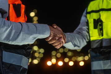 Night scene. Close up of Asian man petrochemical engineers shaking hands together after going through routine checks at petroleum oil refinery in industrial estate.