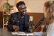 © Seventyfour - Medium shot of cheerful African American man wearing glasses and black suit talking to unrecognizable female guest sitting at table during podcast in studio