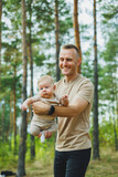 Fototapeta Łazienka - A young dad holds his little son in his arms while standing in the park. Dad is playing with his son