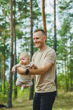 Fototapeta Łazienka - A young dad holds his little son in his arms while standing in the park. Dad is playing with his son