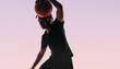 Young male athlete dribbling basketball in studio with pink background
