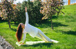 Woman performing yoga side plank on green mat outdoors, surrounded by blooming trees in a vibrant green park, showcasing strength and flexibility