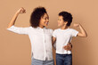 © Prostock-studio - African American woman and a boy are standing next to each other, showing biceps and smiling, isolated on beige background