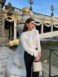 beautiful woman with dark hair in luxurious white silk blouse and black pants and accessories posing by the Alexandre III bridge in Paris
