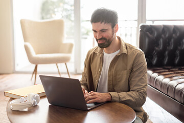 Poster - A man sits at a table, focused on his laptop computer. He appears to be working or studying intently, with papers and a drink nearby.