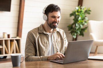 Aufkleber - A man is seated at a table with a laptop open in front of him. He is wearing headphones and appears focused on the screen, possibly working or listening to music online