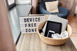 digital detox and technology concept - close up of device free zone words on light box and different gadgets in wicker basket on table at home