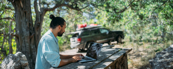 Wall Mural - Male tourist working on a laptop outdoors in a camping.