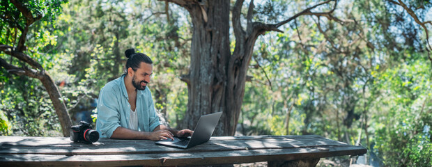 male photographer working on a laptop outdoors in a camping