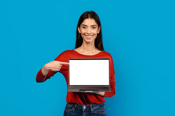 Poster - A woman dressed in a red sweater is holding a laptop with white blank screen in her hands, isolated on blue background, mockup, copy space
