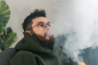 © satura_ - Portrait bearded man is smoking hookah at home and blowing cloud of smoke, copy space and place for text - chill time and resting concept