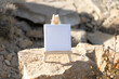 Mockup. White mini canvas on small wooden easel stand standing on cliff rocks outdoors with blurred nature background