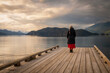 Senior woman gazing out over a lake at sunset from a boat dock. Seen at Harrison Lake, British Columbia, with dramatic clouds and calm waters.