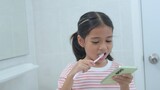 Fototapeta  - A young girl is brushing her teeth while looking at her phone
