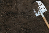 Fototapeta Zachód słońca - Dark black soil ground texture background with copyspace and shovel on garden bed in farm garden. Organic farming, gardening, agriculture