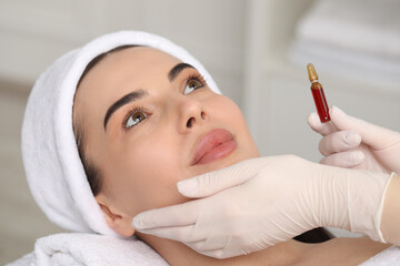 Canvas Print - Professional cosmetologist holding skincare ampoule while working with client in clinic, closeup