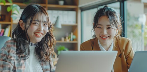 Wall Mural - Two smiling Asian women sit in front of their laptops, exuding happiness and focus in a modern, brightly lit corporate office setting Cinematic Mood and tone.