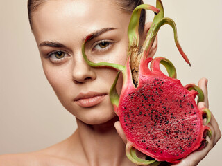 Closeup portrait of beautiful young woman with dragon fruit mask on her face against beige background