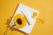 Yellow background against a white bath towel with a unlabeled tube placed above, decorated by sunflower and petals around. Mock up for advertising cosmetic product of sunflower