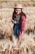 © Satori Studio - Dedicated farmer is attentively checking the wheat stalks while holding a tablet in a sunny, rustic field.