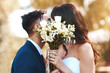 © peopleimages.com - Cover, face and couple with flowers kiss at wedding in celebration of love and marriage. Bride, groom and people show care and support in romantic commitment with floral bouquet outdoor in summer