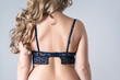 Woman wearing properly fitting bra, female back in a blue brassiere on gray background