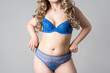 Blonde woman with small breasts in blue lace transparent lingerie on a gray background