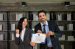 Portrait of two caucasian business woman and man in formal wear holding a certificate of appreciation recieved from business performace competition award winning in modern office.