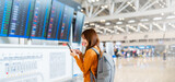 Fototapeta  - Young asian woman in international airport, using mobile smartphone and checking flight at the flight information board