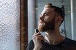 © ALLAI - Young Caucasian man carefully grooming his beard using an electric trimmer in a modern, well-lit bathroom