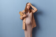 Sad unhappy young adult pregnant woman wearing dress and jacket posing isolated over blue background making facepalm gesture having troubles with documents touching her head
